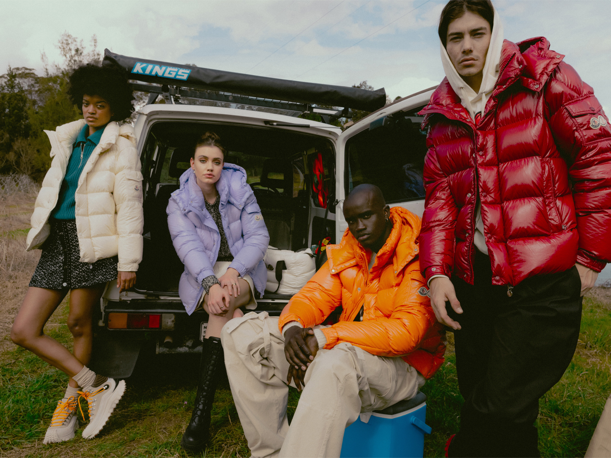 Models wearing puffer jackets posing beside a campervan