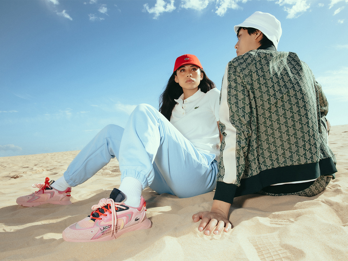 Female and male models wearing Lacoste clothes sitting on sand