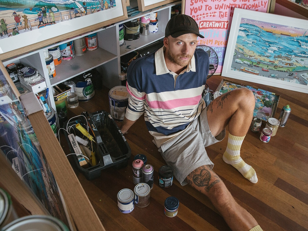 Man sitting on the floor surrounded by paintings and art materials