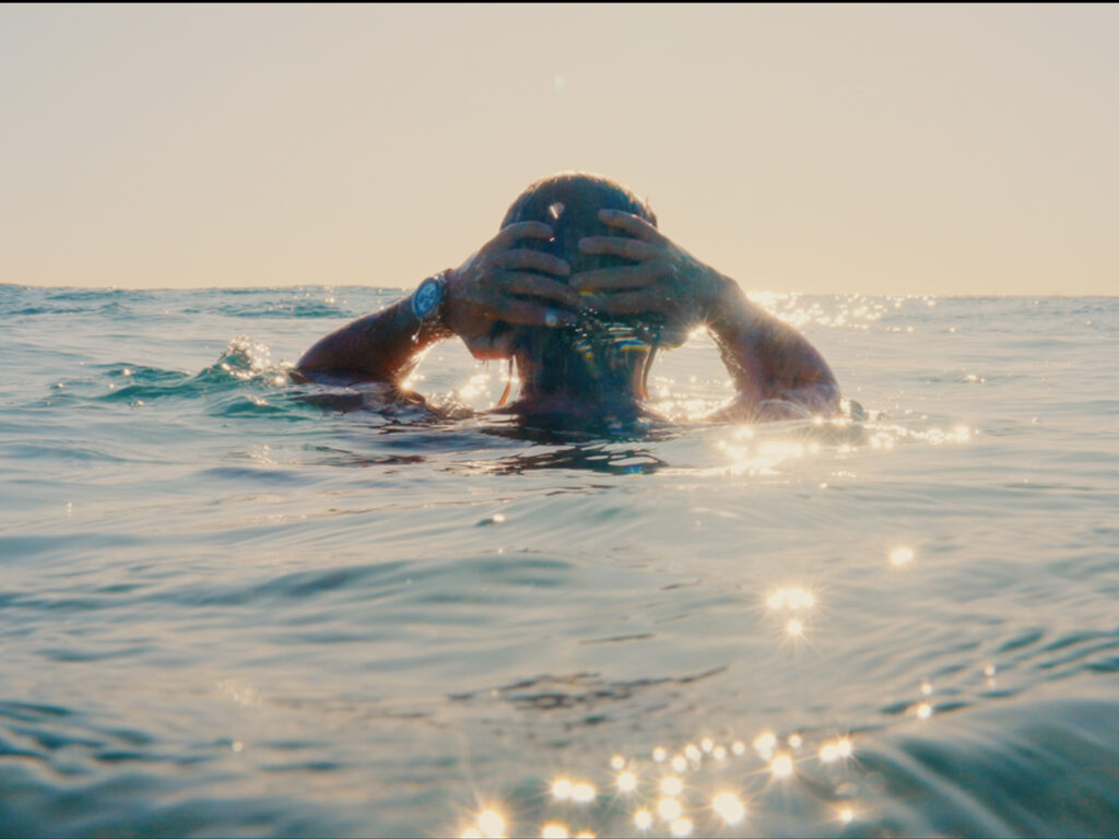 Back view of a man emerging from the sea with both hands on his wet hair wearing a Seiko watch