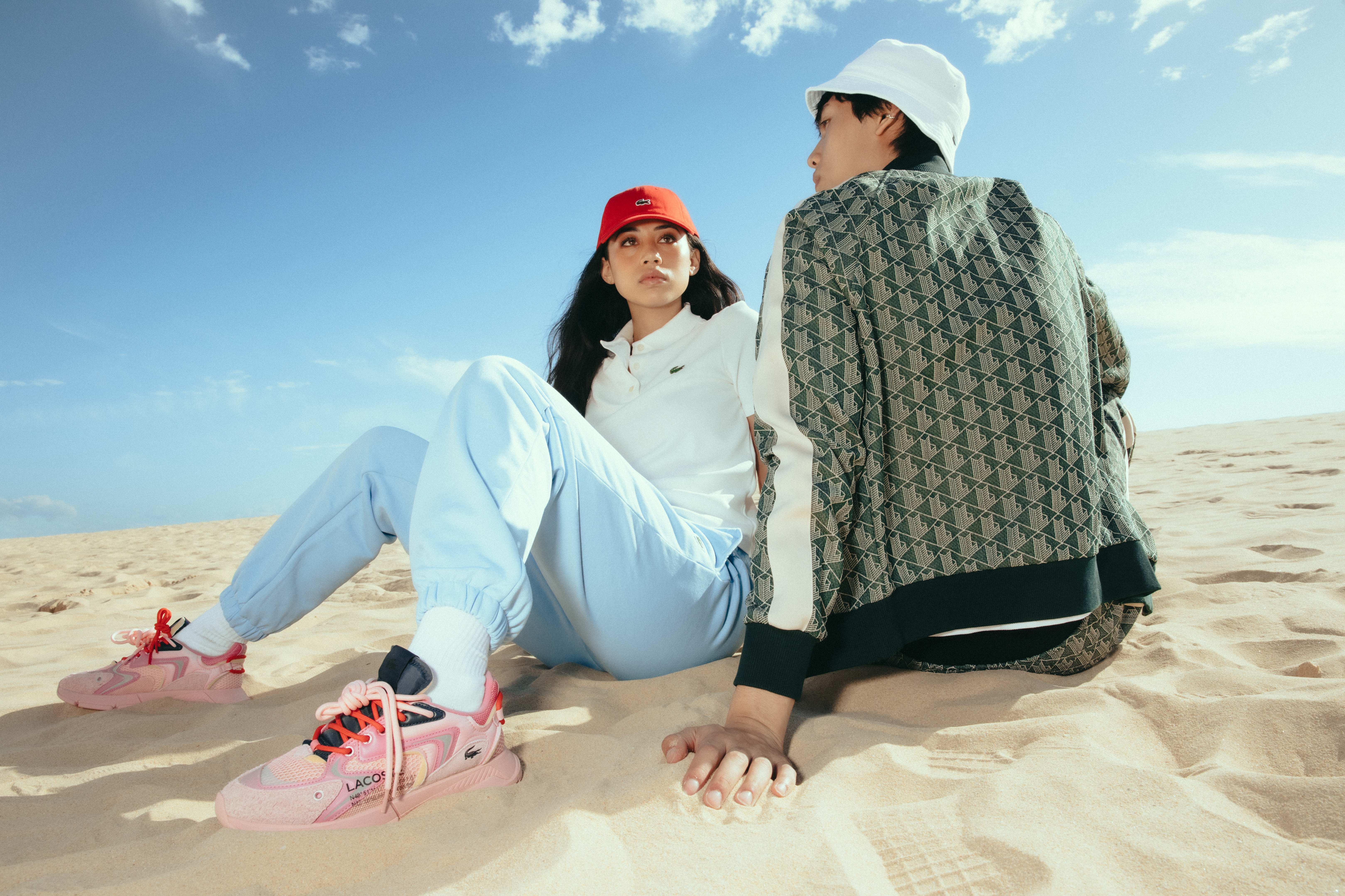 Female and male models wearing Lacoste clothes sitting on sand